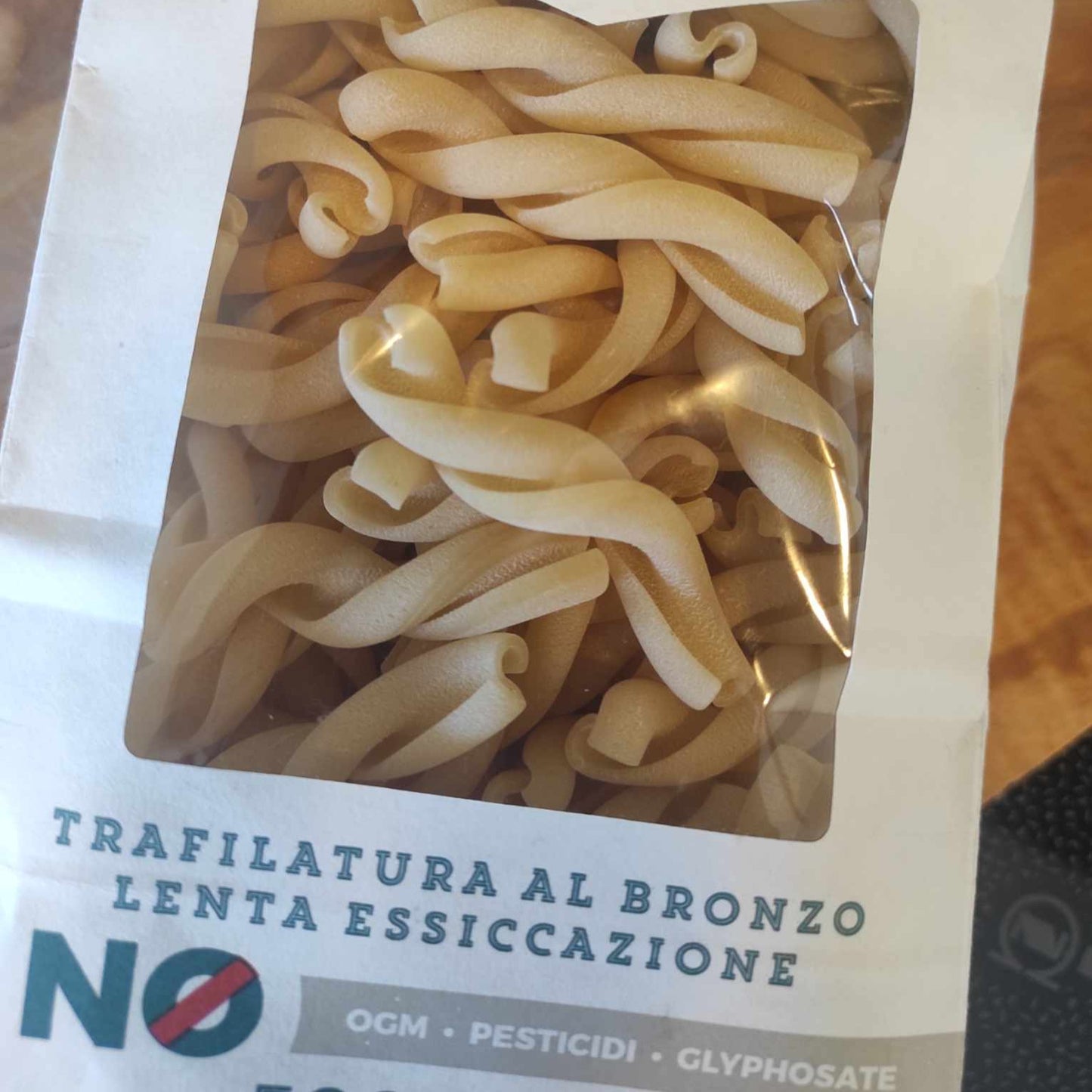 Packung Trecce-Pasta aus Urgetreide mit Aufschrift "Trafilatura al Bronzo" und "Lenta Essiccazione" auf Holzoberfläche.
