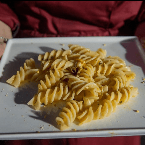 Person, die einen quadratischen weißen Teller mit gekochten Eliche Giganti Nudeln hält; gewürzt mit Kräutern und Gewürzen.