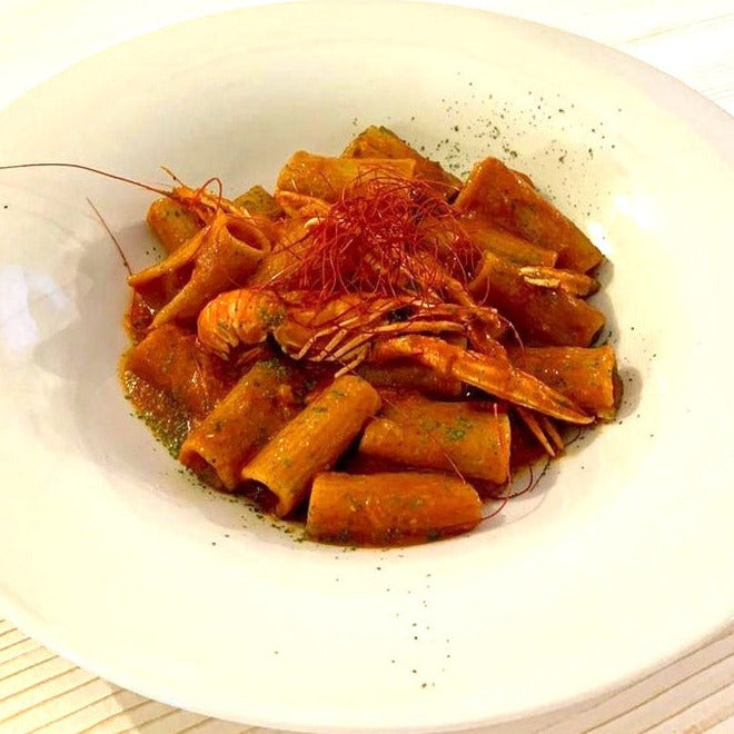 Italienische Kochboxen-Gericht mit Rigatoni-Pasta in Tomatensauce, garniert mit Garnelen und Kräutern in einem weißen Teller.