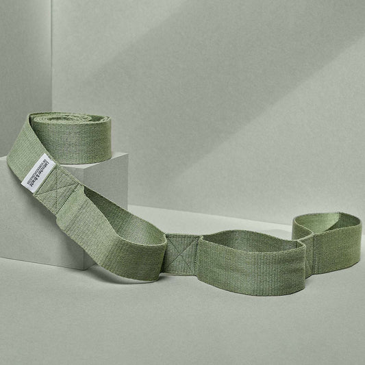 Grüner elastischer Schulterriemen „Der Schulterretter“ auf einem minimalistischen grauen Hintergrund, der sich auf Textur und Design konzentriert.