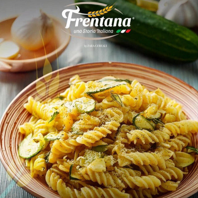 Teller mit Fusilletti aus Urgetreide, dekoriert mit Zucchini und Kräutern, auf Holztisch mit Kartoffeln und einer Zucchini.