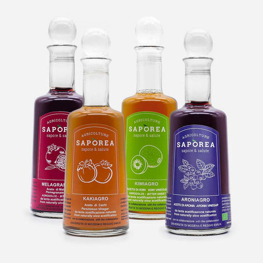 Vier bunte Essigflaschen mit Korkverschlüssen in den Farben Rot, Orange, Grün und Lila. Jede Flasche zeigt Fruchtmotive.