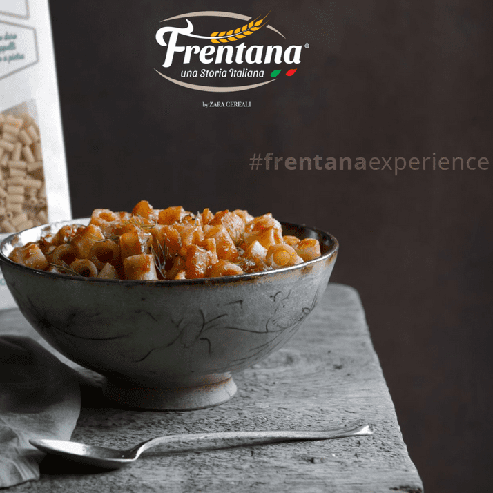 Schüssel mit gekochten Nudeln von Tubetti Rigati auf einer rustikalen Fläche, im Hintergrund eine Schachtel mit der Aufschrift „Pasta aus Urgetreide“, daneben ein Löffel.