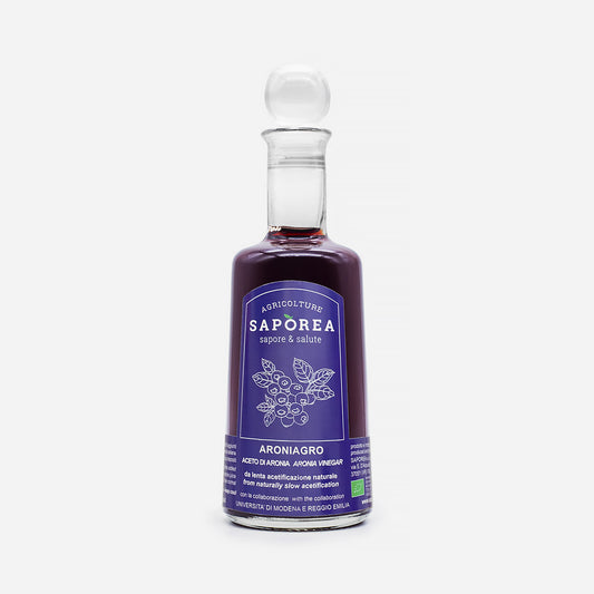 Flasche Aronia-Essig mit klarem Verschluss, violettem Etikett mit Aronia-Beeren, hervorgehobene hochwertige Essigqualität.