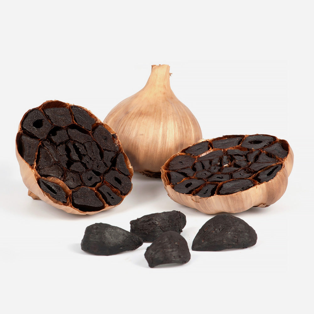 Eine aufgeschnittene schwarze Knoblauchknolle, die reiche, tiefe Farben zeigt, umgeben von schwarzen Knoblauchzehen auf weißem Hintergrund.