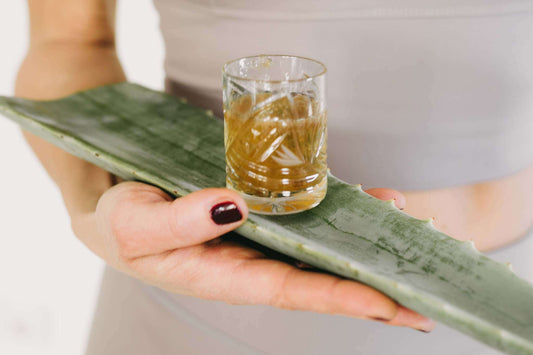 Eine Person hält ein großes Aloeblatt mit einem Glas Aloe-Vera-Saft in der Hand.